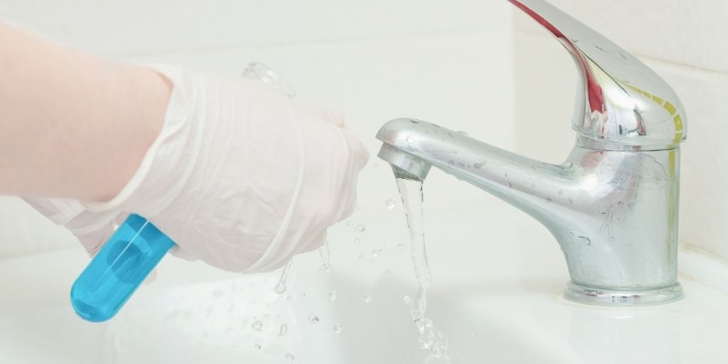 A person's hands holding a test tube under a sink faucet to test for water cleanliness